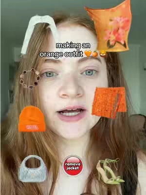 A selfie of a young woman with fair skin and long reddish-brown hair, looking at the camera. Around her head, various orange outfit pieces are digitally placed as if choices or suggestions. These include a small orange beanie, an orange top, a pair of orange shorts, a bracelet, white jeans, an embellished handbag, and a pair of high-heeled shoes. Text reading "making an orange outfit," is above her head, along with emoji heart and a peach emoji. A circular button with red background and the words "remove jacket" sits below her.