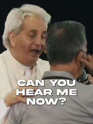 The image features two men close to each other. The man on the left has white hair and is looking down at the man on the right, who has dark hair and is wearing glasses. Text overlayed on the image reads, "CAN YOU HEAR ME NOW?"