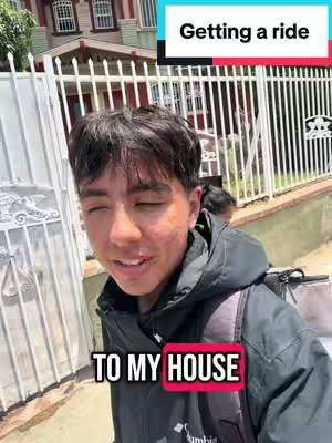 A young man stands outside a white fence with a house visible in the background. The man is facing forward, smiling slightly, with text overlays at the top and bottom of the image. He is wearing a black jacket.