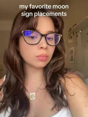 A young woman with brown hair and glasses is centered in the frame. The text "my favorite moon sign placements" is overlaid at the top. The background is soft, slightly out of focus with some decorations visible.