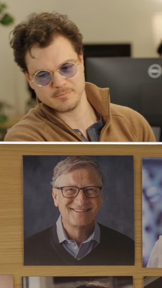 The cover image is a composite. The top half features a man with curly brown hair, wearing round, blue-tinted glasses and a brown zip-up jacket over a blue shirt. He is looking slightly off-camera, smiling subtly. The other half of the image is a shot of Bill Gates. The image of Bill Gates is a portrait photo pasted onto a wooden background. The composition is simple, with a wooden surface and a blurry background with various blurred photographs.