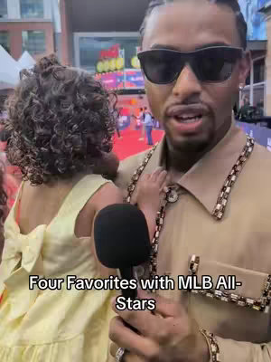 A man wearing sunglasses holds a small child, with a microphone in front, set against an urban outdoor background. The text overlay indicates a topic related to MLB All-Stars.