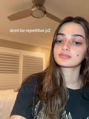 A selfie-style shot featuring a young woman facing the camera. The background includes a white ceiling with a ceiling fan and a visible window with closed blinds. The woman has long brown hair and is wearing a black top. Text overlayed at the top reads 'dont be repetitive p2'.