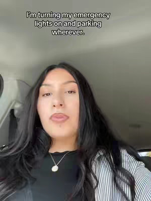 A selfie-style video is presented, taken from inside a car. The creator, a woman with long black hair, is centered in the frame. She's wearing a black top and a striped overshirt, with a necklace visible. The background is the car's interior and includes the ceiling. Overlay text communicates the video's context.