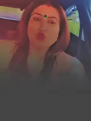 The cover image features a woman in a car with pink lipstick and a bindi between her eyebrows, looking at the camera and making a kissing face. It's a selfie-style shot in what appears to be a car setting. The top half of the image is clearly in focus, while the bottom half blurs out into darkness.