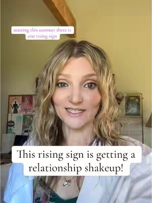 A woman with long blonde wavy hair smiles directly at the camera. She wears a white top over a floral top and a necklace. Text overlays appear at the top and bottom of the frame in white boxes. The background includes a wooden beam and framed pictures, suggesting an indoor setting.