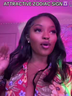 The cover image features a woman in a brightly lit room with pink and purple lighting. The woman is looking towards the right of the frame with her mouth open as if speaking. She has long, dark hair. The image is framed from the chest up, and she's wearing a floral patterned top. Text overlayed on the top of the image reads "ATTRACTIVE ZODIAC SIGN".