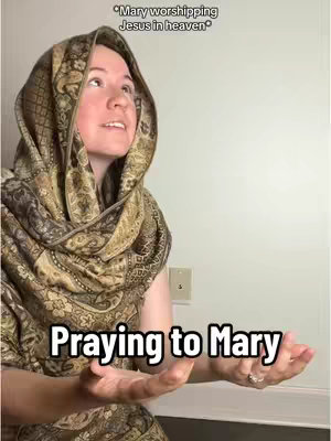 A woman with fair skin wearing a patterned scarf over her head and shoulders, and holding her hands up as if in prayer. Text overlays read "*Mary worshipping Jesus in heaven*" above her head and "Praying to Mary" below. The background is a neutral wall.