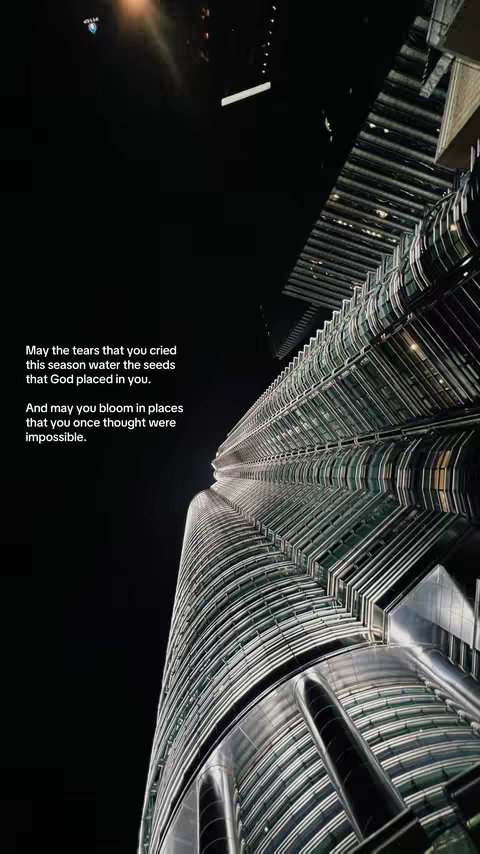 An eye-level, low-angle shot of a skyscraper at night. The building's facade is a mix of glass and metal, with a curved, ribbed design that catches the ambient light. A black sky fills the upper portion of the frame, with text overlaid in white text.