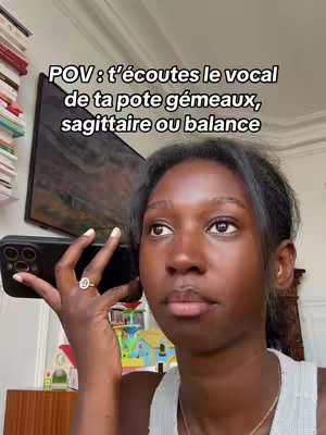 A young Black woman is holding a phone to her ear, looking at the camera with a slightly skeptical expression. Overlay text and part of a framed picture along with other elements in the background are visible.