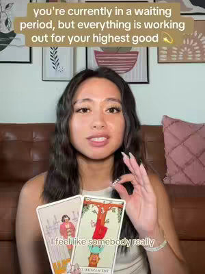 A young woman is centered, holding tarot cards, gesturing with her right hand, and speaking. Above her head is a text overlay, and the background includes framed artwork and a couch. The image is well-lit.