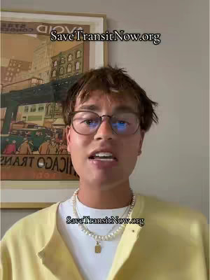 A man with glasses is speaking to the camera. Behind him is a framed picture with a vintage theme. The man has short brown hair and is wearing a white undershirt with a yellow cardigan, and a pearl necklace with a gold pendant. The text SaveTransitNow.org is layered repeatedly on the video.