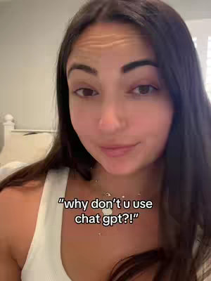 A medium shot shows a young woman with long dark hair. Her expression is gentle as she seems to be speaking. The background is soft, with a glimpse of a headboard and window blinds. Text overlay is visible, "why don't u use chat gpt?!"