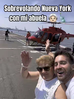 A selfie-style image with two people in the foreground, and a red helicopter and New York City scene in the background. The main focus is on a man and an older woman. The woman is wearing sunglasses and a white top, and the man is smiling. Above the helicopter is a cartoon depiction of an older woman with a white hair and a small Statue of Liberty.