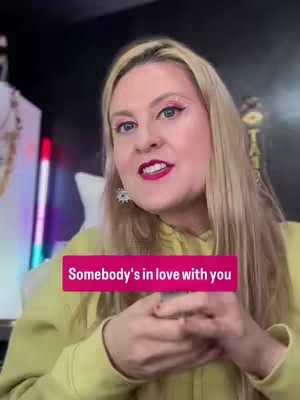 A woman with blonde hair and pink eyeshadow in a yellow hoodie, speaking to the camera with a text overlay that reads, "Somebody's in love with you."