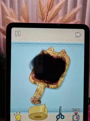 An iPad displaying an interactive game interface. A cat-shaped object with a dark central element is the main focus. Below are icons for a roll of tape, scissors, and a clock.