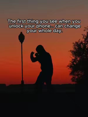 Silhouette of a person in a boxing stance against a vibrant orange and purple gradient sky, with a tall, slender street lamp to the left and a tree to the right. Text overlayed at the top reads 'The first thing you see when you unlock your phone... can change your whole day.'