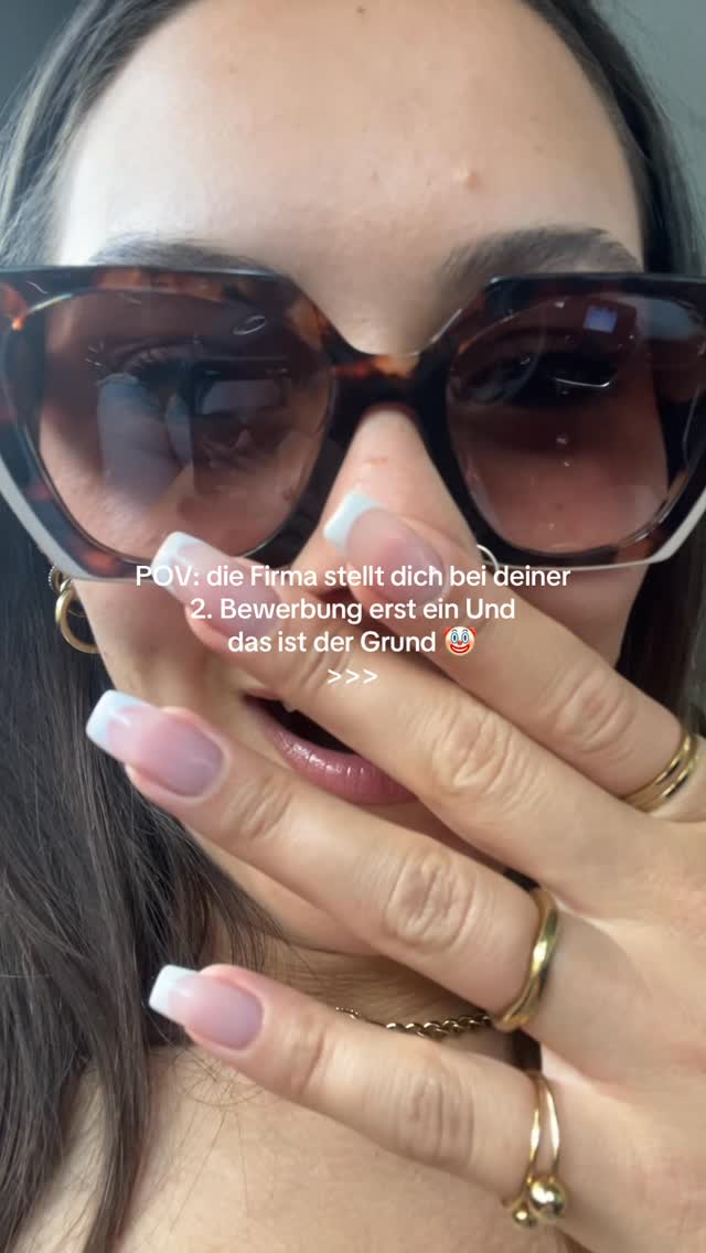 A close-up shot featuring a person wearing large, brown-tortoiseshell sunglasses. The individual's hand, with long, manicured nails painted with a white tip, is covering their mouth, revealing part of their lips and some gold rings. The background is blurred, suggesting this is a selfie.