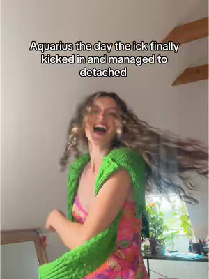 The image features a woman with long, wavy hair in motion, laughing heartily. She is wearing a brightly colored dress and a green knitted shrug or shawl. The background is an interior space with a window visible through which a glimpse of the outside.