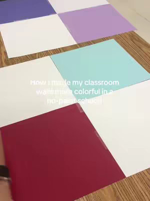 The cover image shows a close-up view of a wooden surface upon which colorful square paper sheets are arranged. The sheets are in a checkerboard pattern, with alternating colors visible: white, red, purple, light purple, and a light teal blue.