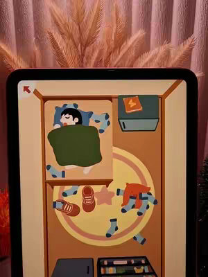 An ipad screen displaying a cartoonish, top-down view of a room. A person is sleeping in bed, surrounded by scattered objects, like shoes and socks. The background is a soft pink, and there is a decorative brown plant at the top of the screen.