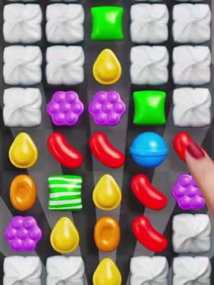A close-up image of a mobile game interface resembling a match-three puzzle. Various colorful candies and shapes are arranged in a grid; a finger with red nail polish interacts with the game board.