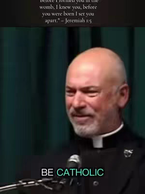 A medium shot features a fair-skinned man wearing a black clerical collar and dark jacket. He is positioned in front of a dark-green draped backdrop. Text at the top states a bible quote. The man is smiling and in the bottom part of the image declares "BE CATHOLIC".