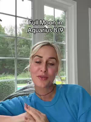 A woman is in front of a window. The overlaying texts read "Full Moon in Aquarius 8/9". The background is a combination of clear sky and green trees and the window's frame.