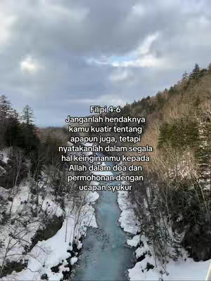 A landscape view featuring a river flowing through a valley flanked by snow-covered banks and wooded hills. The sky is overcast with a few glimpses of light. Overlayed text in Indonesian is featured in the upper center, providing a verse from Philippians 4:6.