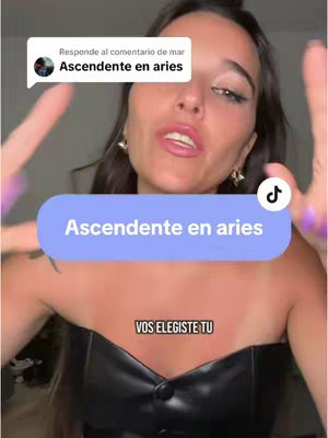 A woman with dark hair and light skin is centered in the frame. She is wearing a black leather top and gold earrings. Her hands are raised, fingers spread, in a gesture suggesting emphasis. A light blue rectangular banner lies on the bottom half of the screen with white text that reads: 'Ascendente en aries.' Beside the banner is the TikTok logo. Above the banner is the text 'VOS ELEGISTE TU'. Above this scene, a comment is visible: 'Ascendente en aries'.