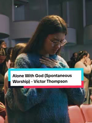 The image shows a woman in a church or similar setting. She is wearing glasses, and a blue sweater, and has her hands clasped over her chest as if in prayer. A text box at the bottom displays the video title and creator.