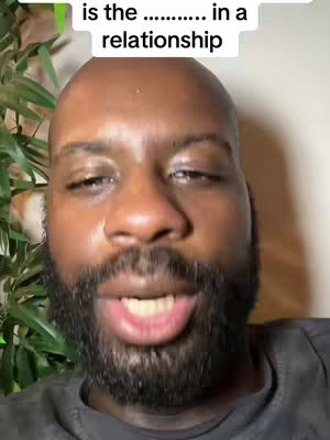 A close-up shot of a Black man with a bald head and a well-groomed beard. He has a neutral expression with his mouth slightly open. In the background, there is some green foliage. The top of the image has text overlayed.