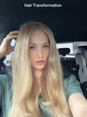 A young woman with long blonde hair is seated inside a car. She is looking directly at the camera with a slight smile, with the text 'Hair Transformation' at the top of the screen.