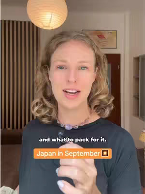 A woman with fair skin and curly blonde hair is centered in the frame, with a bright ceiling lamp above her. She is wearing a black shirt and a purple necklace. Text overlays at the bottom read 'and what to pack for it.' and a highlighted banner that reads 'Japan in September' with the japanese sun symbol.
