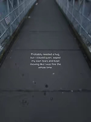 A dark, slightly desaturated shot down a concrete path between two parallel metal structures. The path recedes into the distance, creating a vanishing point in the frame. Text appears in the lower right corner, overlaid on the darker pavement.