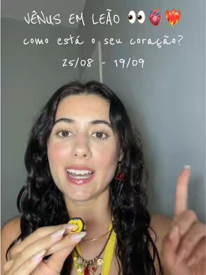 A woman with long, dark hair, wearing earrings and a yellow strap or top, is smiling and pointing her right index finger upwards. She is holding a yellow smiley face pin. Above her, text is overlaid on the image, along with several emojis including eyes, a heart, and a flaming heart.