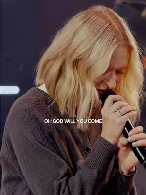 The image features a woman with long blonde hair holding a microphone. She appears to be singing or praying, with her head bowed and eyes closed. The lighting suggests a concert or church setting. The text overlay reads, "OH GOD WILL YOU COME."