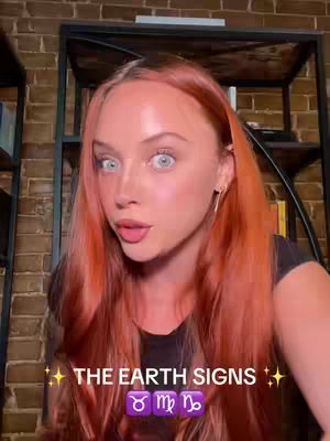 A woman with auburn hair looks directly at the camera with a surprised expression. Below her, the text overlay reads: 'The Earth Signs' with symbols for Taurus, Virgo, and Capricorn.