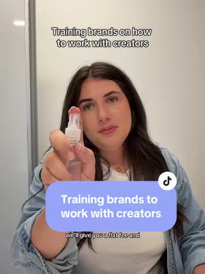 A woman is holding a clear spray bottle, facing the camera in a studio setting. Above her is text that says, 'Training brands on how to work with creators.' Additionally, a blue box with white text provides another hook and caption in the bottom left hand corner.