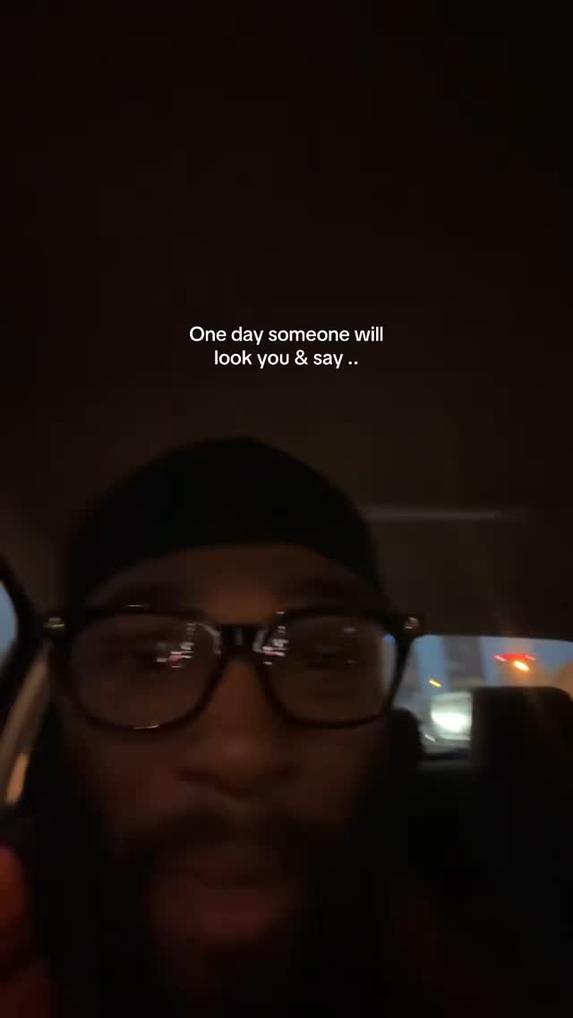 A selfie-style video from inside a car. The person in the video, a man with glasses and a black cap, is looking at the camera. The background appears to be dark, possibly night time or a dimly lit interior.