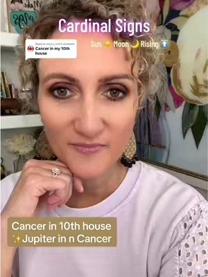 A woman with light skin and curly blonde hair is centered in the frame, looking towards the camera with a slight smile. She wears makeup, including eyeshadow and lipstick, and is adorned with large, ornate gold earrings. A ring with a noticeable stone is on her left hand, and her white top is partially visible. Text overlays at the top read "Cardinal Signs" with related icons. Additional text boxes offer astrological insights about the "10th house" and "Jupiter in Cancer". The background is slightly blurred, with a glimpse of a floral arrangement and shelves.