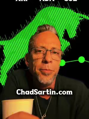The cover image presents a medium shot of a man with glasses and a beard, holding a white cup. Behind him, a green bull graphic and a data graph are visible against a black background. Text at the top indicates 'XRP ADA SOL', and website text at the bottom says 'ChadSartin.com'. The color scheme is dominated by black and green, highlighting the financial theme.