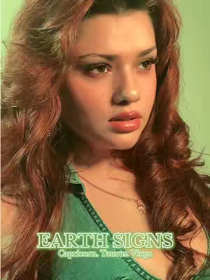 A close-up of a woman with wavy auburn hair and subtle makeup. The woman is looking off-camera with a slight pout. She wears a green denim top and a gold necklace. Text that reads "EARTH SIGNS" in a green neon font appears across the bottom of the image, with the zodiac signs "Capricorn, Taurus, Virgo" written below.