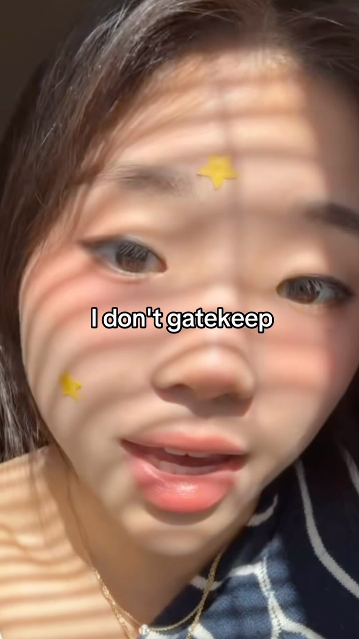 Close-up shot of a person's face, partially lit by sunlight casting shadows. The person has light skin, dark hair, and is wearing a gold necklace. Two yellow star stickers are placed on the face. The text overlayed on the picture says "I don't gatekeep".