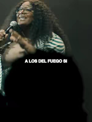 A woman with curly dark hair and glasses holding a microphone, singing or speaking in a dark setting. The hook text in Spanish is overlaid in the lower portion.