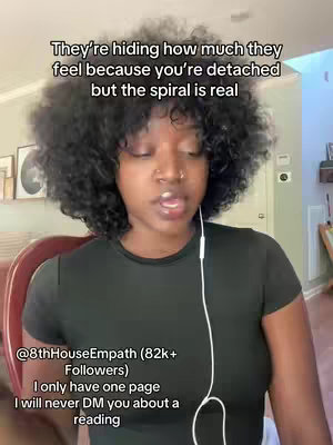 A medium shot features a Black woman with curly hair addressing the camera directly. The upper portion of the image contains overlaid white text on a black background. The woman is wearing a black top and earbuds and appears to be in a well-lit indoor setting with paintings and home decor in the background. She is likely talking to the camera.