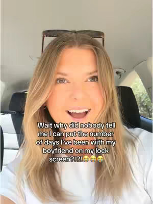 A woman with blonde hair and a white shirt is sitting in a car. There is overlaid text in black at the bottom. She is smiling and looking at the camera.