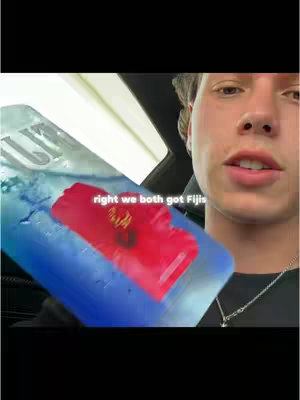 A young man in a car holds up a Fiji water bottle with a red flower design superimposed on it. Text overlay says 'right we both got Fijis'.