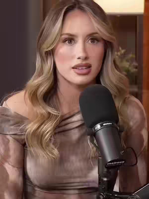 The cover image features a woman with long, wavy blonde hair, looking directly at the camera. She is holding a microphone in front of her, suggesting a podcast or interview setting. The background is slightly blurred, with warm tones.