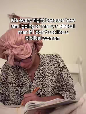 A person wearing a pink silk bonnet and a leopard-print button-up shirt is sitting in a bed with a notebook and pen. Text overlayed states: "Me every night because how am I going to marry a biblical man if I don't act like a biblical women."